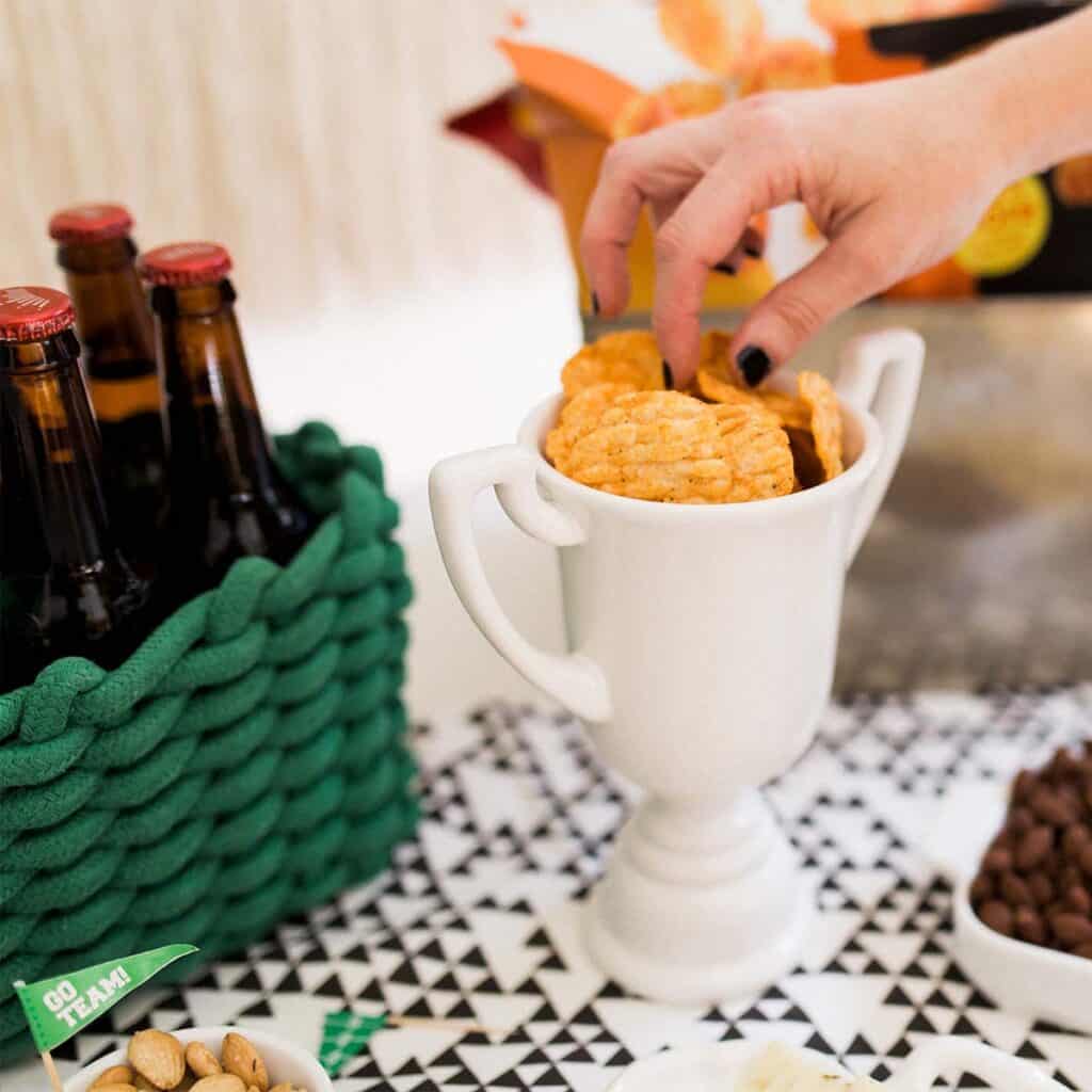 Woman taking a chip from a ceramic trophy snack dish at a football party.