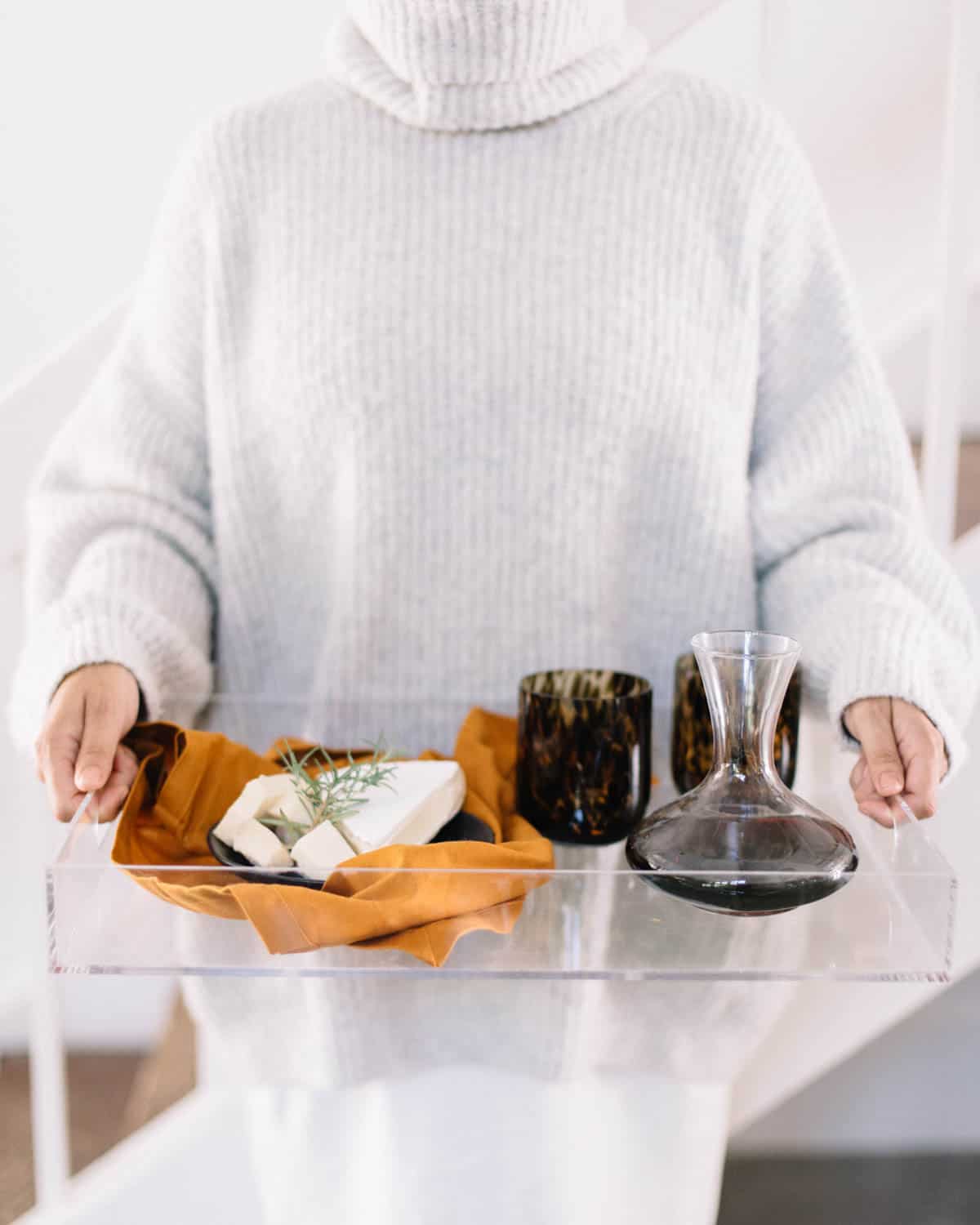 Woman holding an acrylic tray with red wine in a decanter and a cheese board.