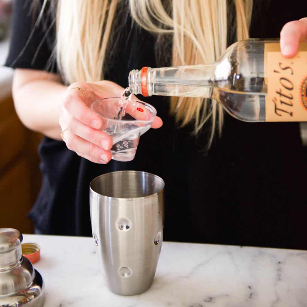 Close up of a woman measuring vodka for a cocktail.