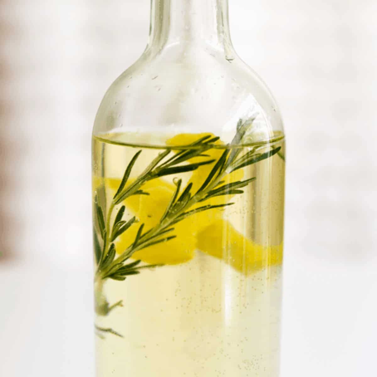 Close up of a bottle of white wine with lemon peel and rosemary sprigs in it.