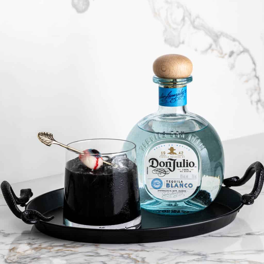 A black drink for Halloween on a tray next to a bottle of Don Julio tequila.