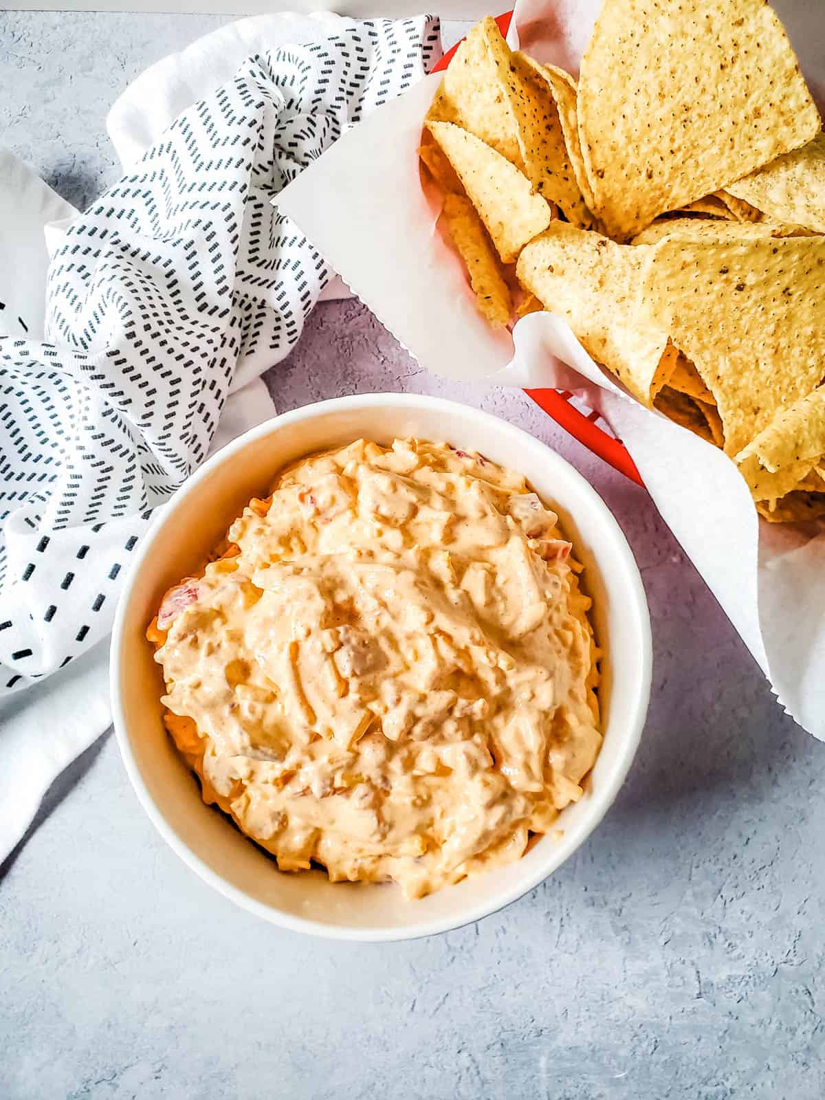 Cream cheese and rotel taco dip in a white bowl beside corn chips.