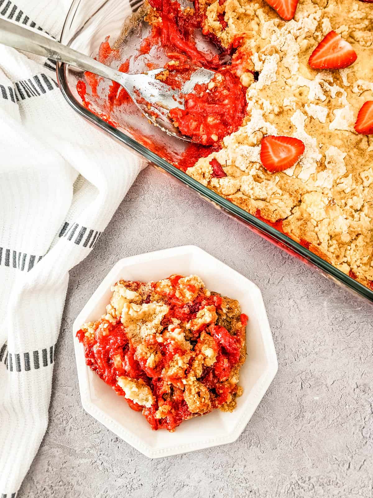 Strawberry Cheesecake Dump Cake in a baking dish with a serving in a white dessert bowl.