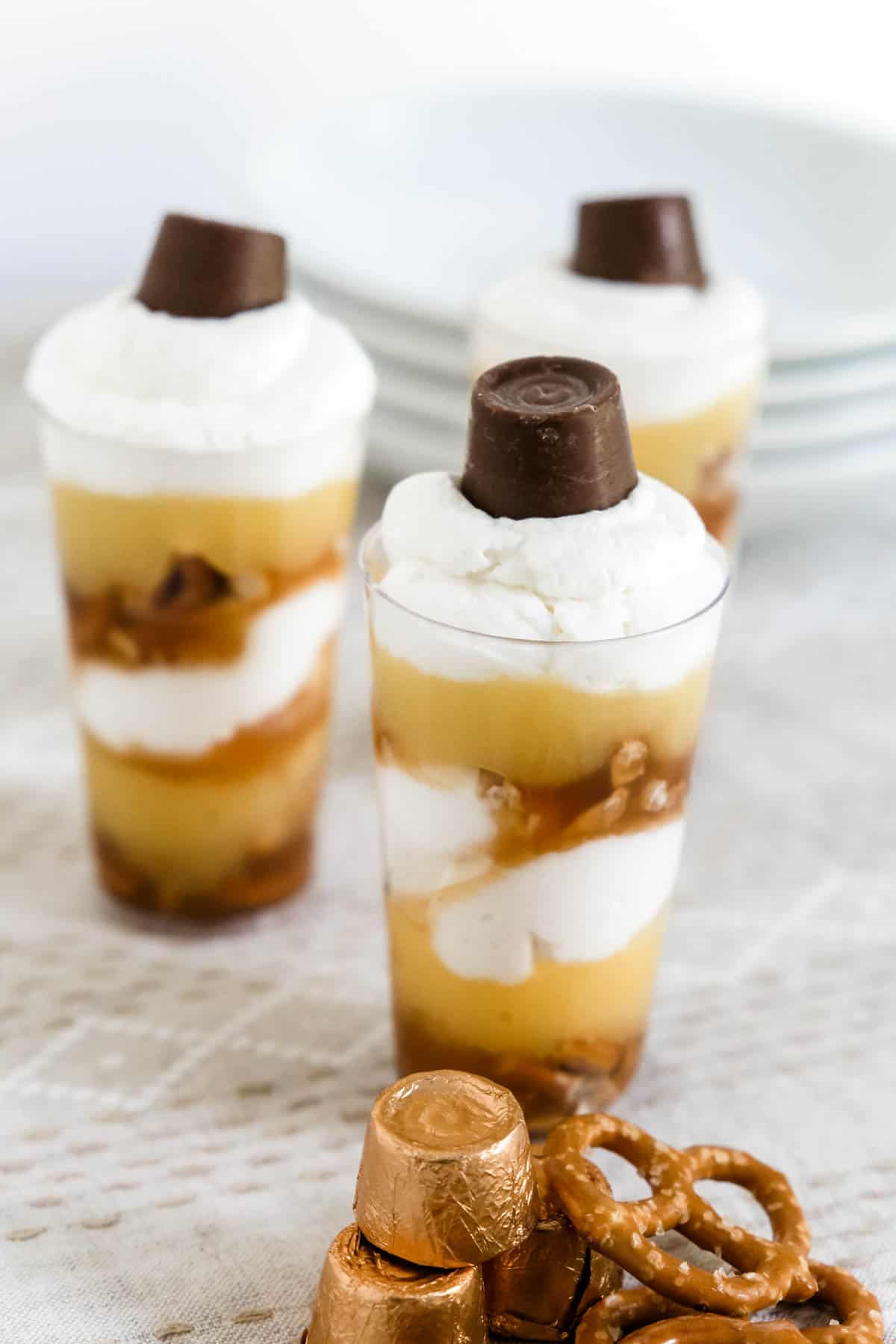 Three small cups of Caramel Pretzel Mini Trifles made with whipped cream topped with chocolate candies.