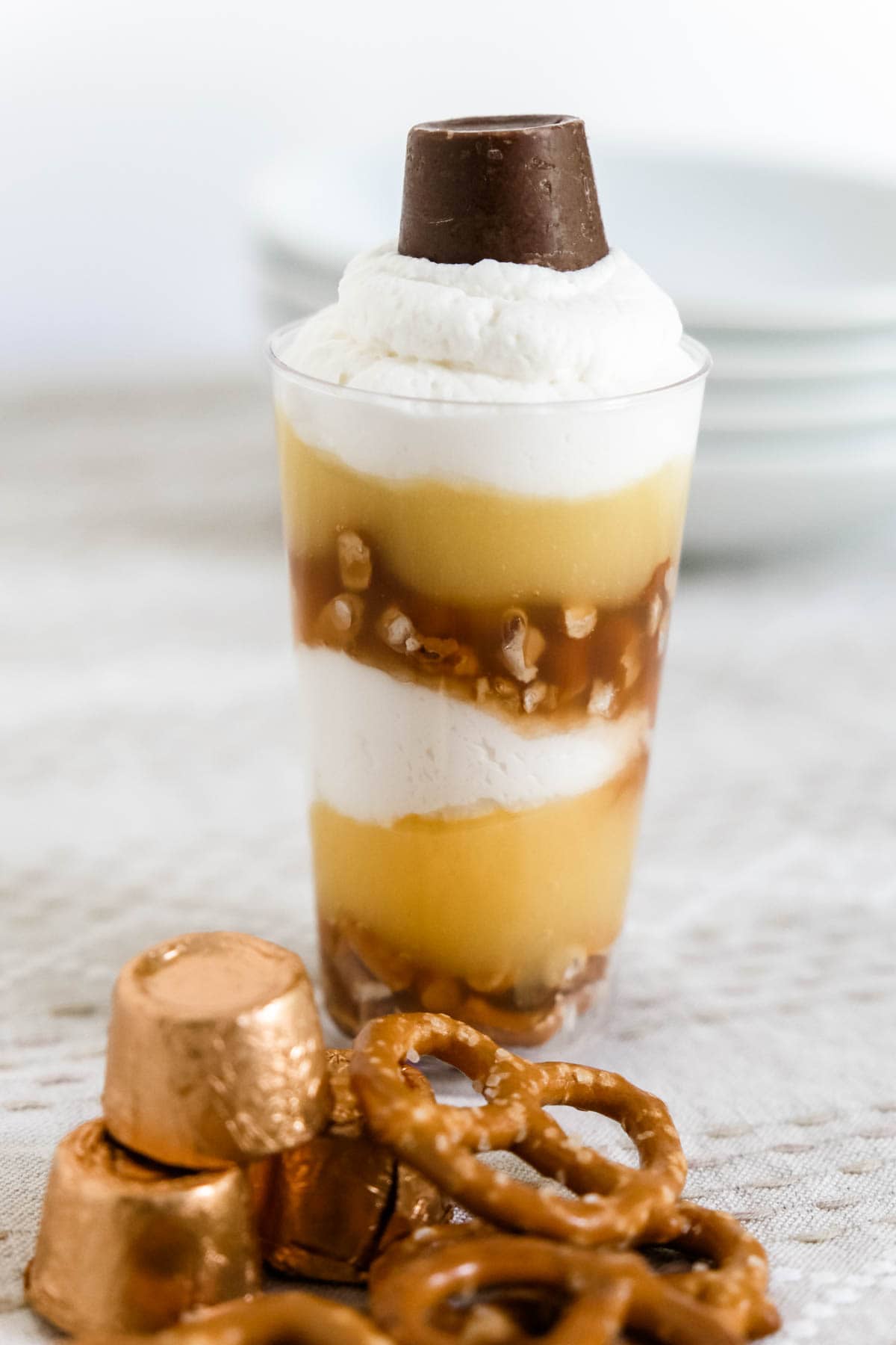 A serving cup of Caramel Pretzel Mini Trifles with chocolate candy topping and some pretzels on the side.