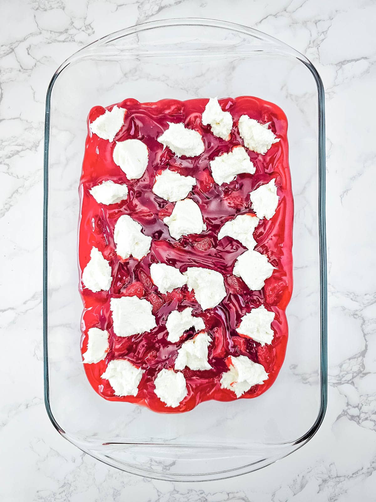 Drops of the cream cheese mixture added on top of the strawberry pie filling layer in a baking dish.